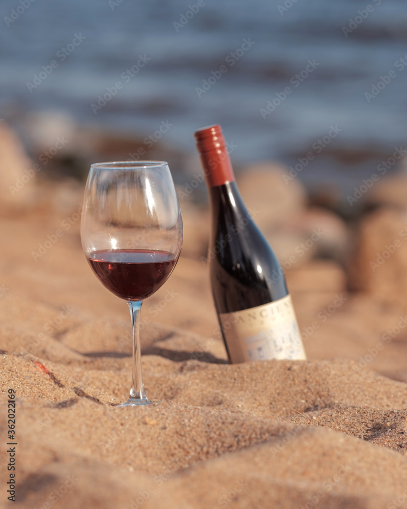Red wine glass with bottle on the beach sand. Summertime, vacation, weekend