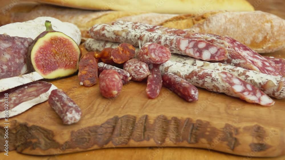 Panorama of delicious dry sausages laying on a wooden board with figs and baguettes Panorama of delicious dry sausages laying on a wooden board with figs and baguettes