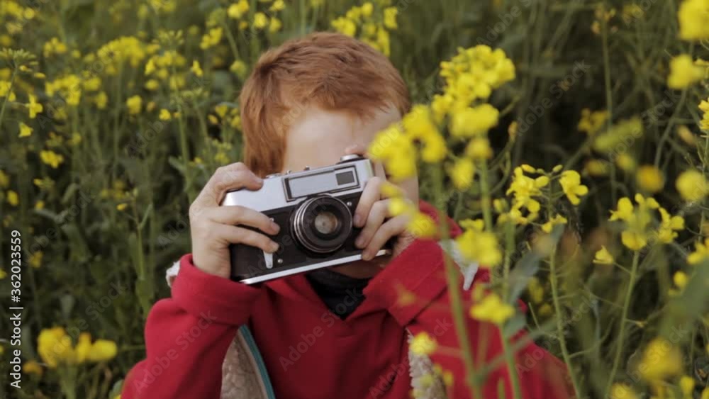 Calm boy taking photo on retro camera while strolling in rapeseed field Calm boy taking photo on retro camera while strolling in rapeseed field
