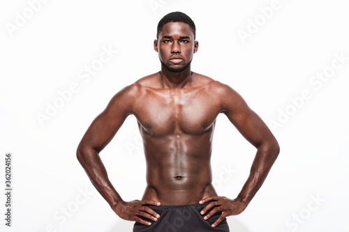 Bare chested black fitness man looking at camera wearing sport short trousers and posing his hands on his hips