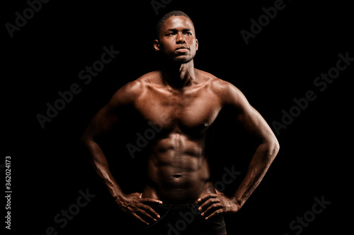 Bare chested black fitness man looking to his left wearing sport short trousers and posing his hands on his hips