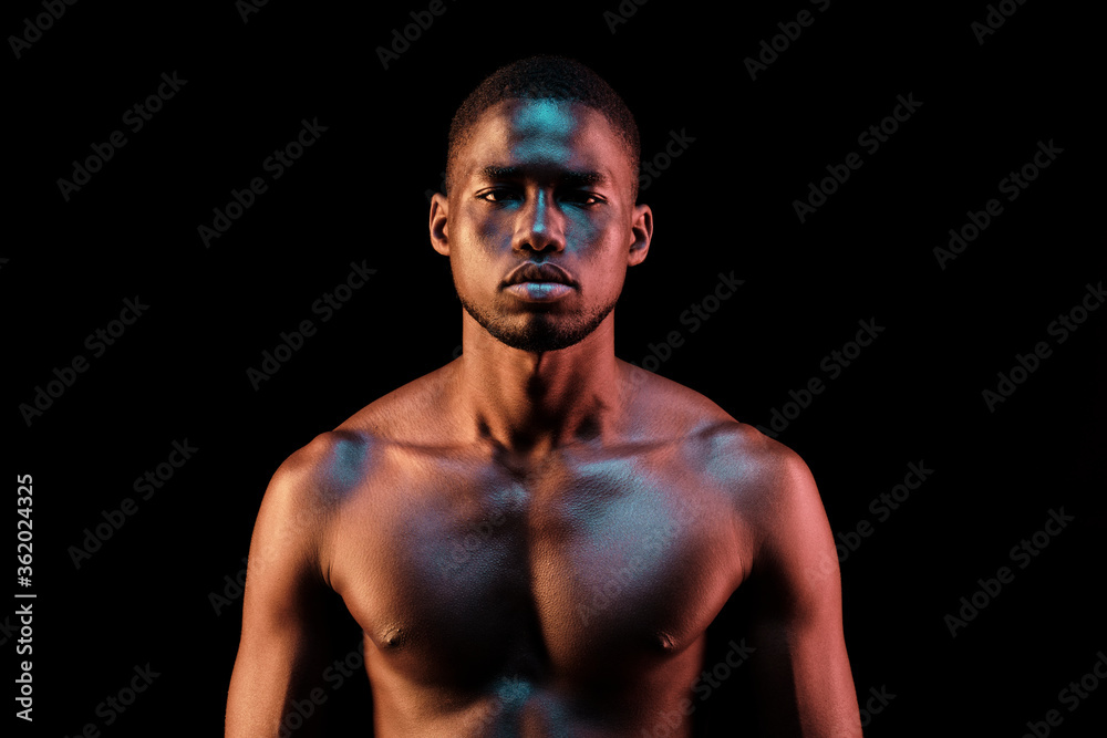 Standing black man looking at camera lit with colored lights Standing black man looking at camera lit with colored lights