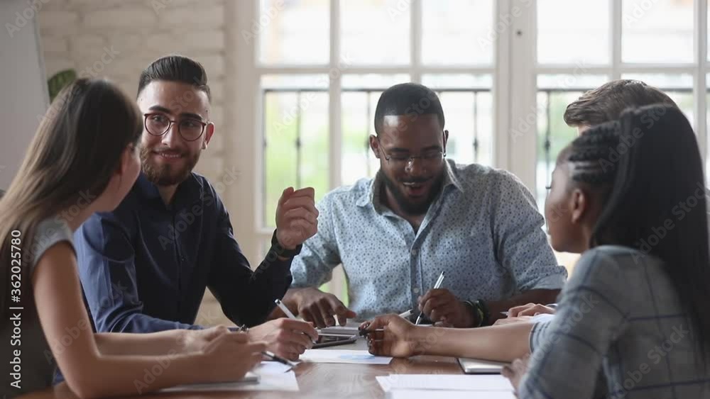 Happy friendly diverse startup team people talking laughing doing paperwork noting working together in successful teamwork share creative ideas sit at office meeting table at group corporate briefing