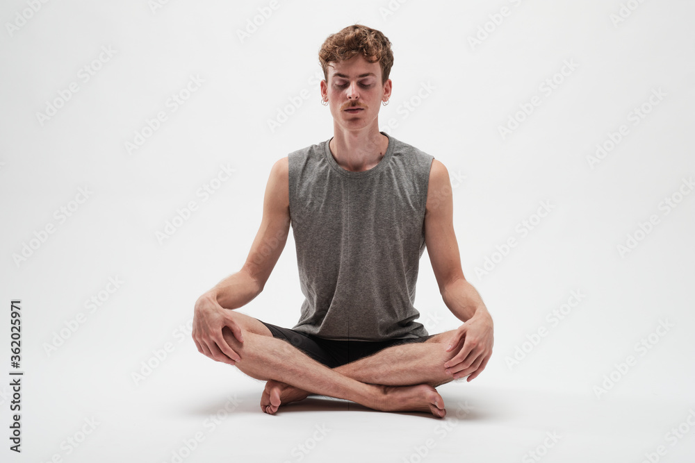 Fototapeta premium Young boy meditating with eyes closed and legs crossed on white background