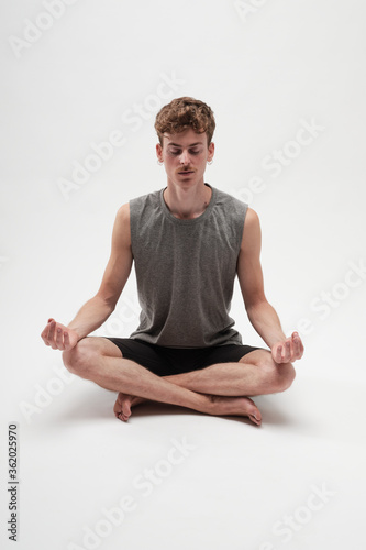 Young boy meditating with eyes closed and legs crossed on white background