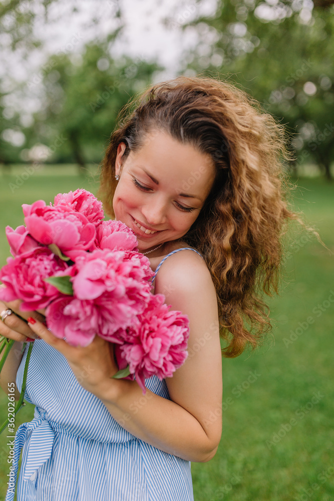 Fototapeta premium girl model mother on her head curly curls holding peonies and flowers in her dress gently presses them to herself on the nature in the park