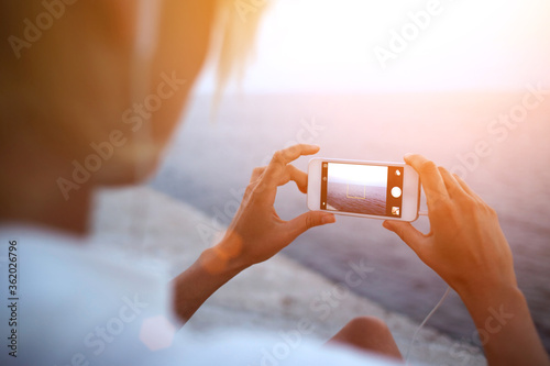 Cropped image of female tourist making photo of beautiful sea view on cell telephone during summer adventure, woman taking picture of ocean landscape on her mobile phone while standing on the beach