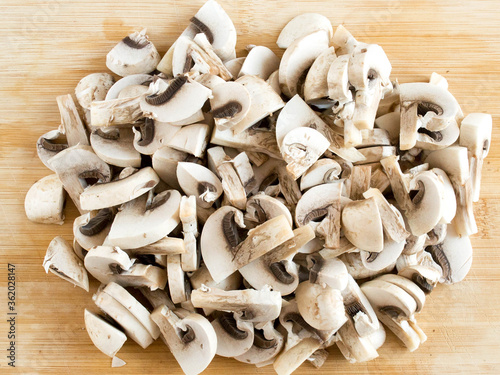 Sliced champignons on a wooden board. Edible mushrooms in pieces, top view