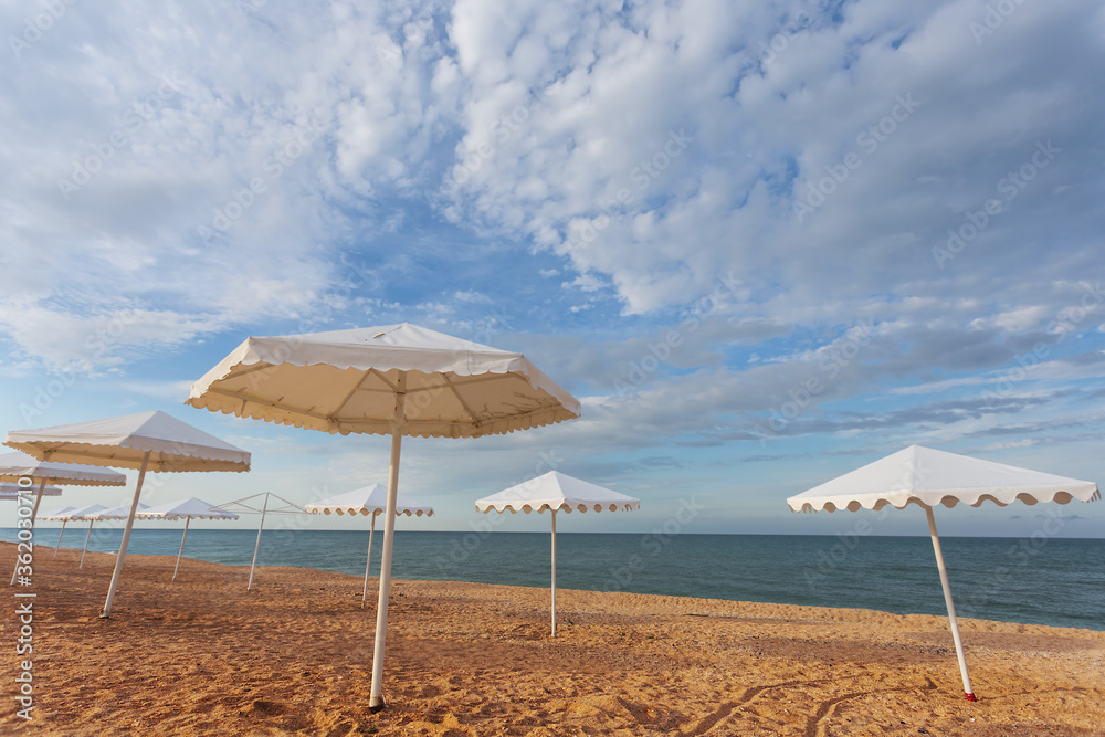 Fototapeta premium white sun umbrella stay on a sandy beach, summer sea vacation background