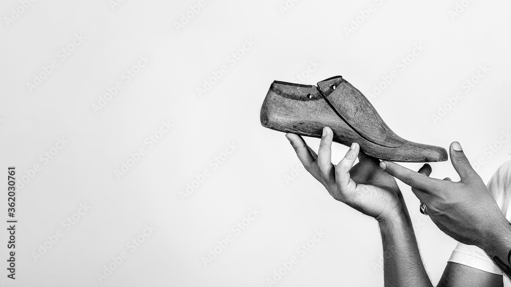Shoemaker holding wooden footwear. Copy space. Man hands holding last shoe.