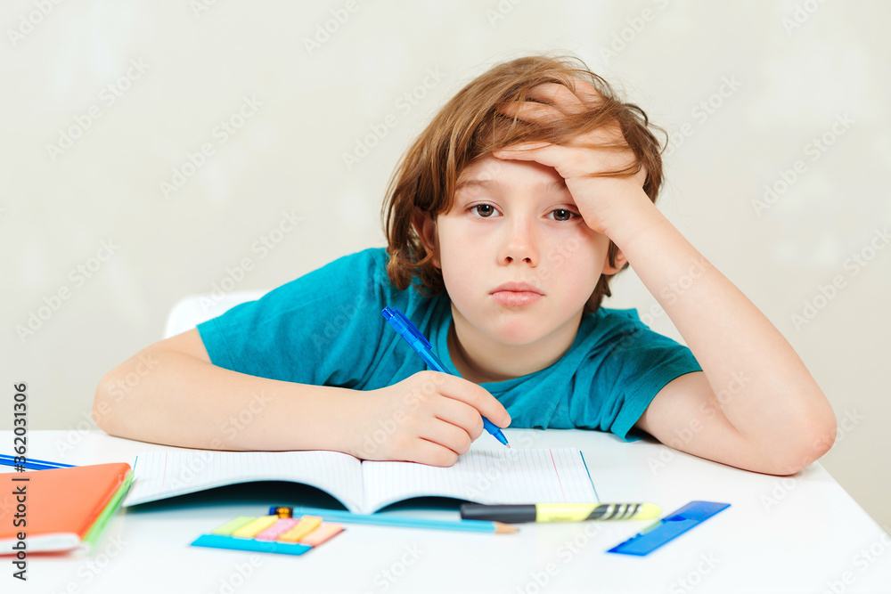 Tired schoolboy sitting at table. Boy doing homework. Learning difficulties, education concept. Tired schoolboy sitting at table. Boy doing homework. Learning difficulties, education concept.