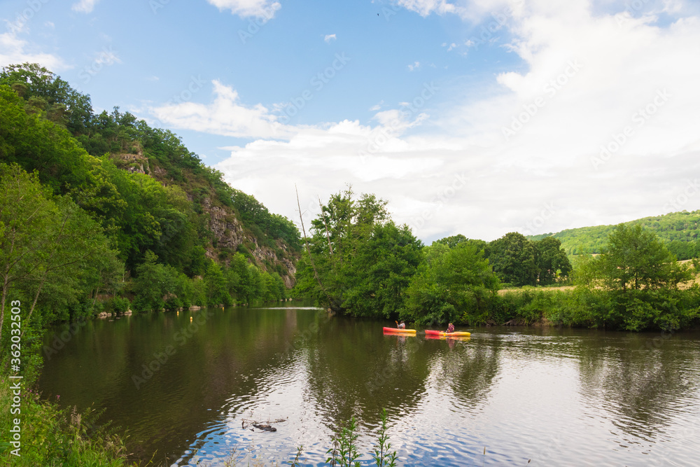 Beautiful landscape in Clécy (Normandy, France). People are kayaking/canoeing on the Orne River. We can see cliffs & verdant nature in the background. Beautiful landscape in Clécy (Normandy, France). People are kayaking/canoeing on the Orne River. We can see cliffs & verdant nature in the background.