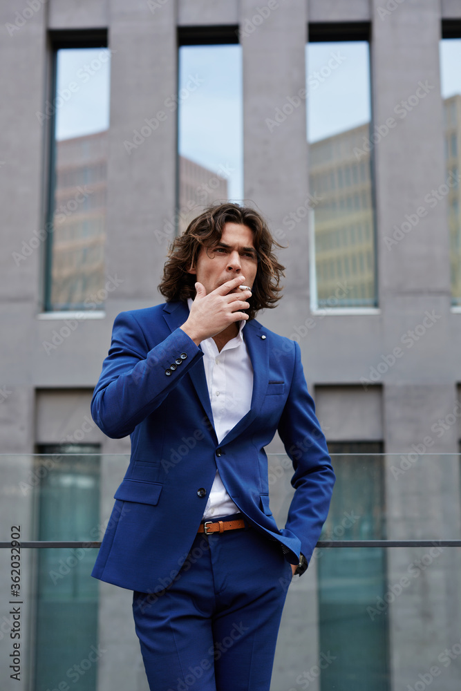 Portrait of classy gentleman smoking a cigar standing outdoors, handsome executive smoking cigarette during his work break Portrait of classy gentleman smoking a cigar standing outdoors, handsome executive smoking cigarette during his work break