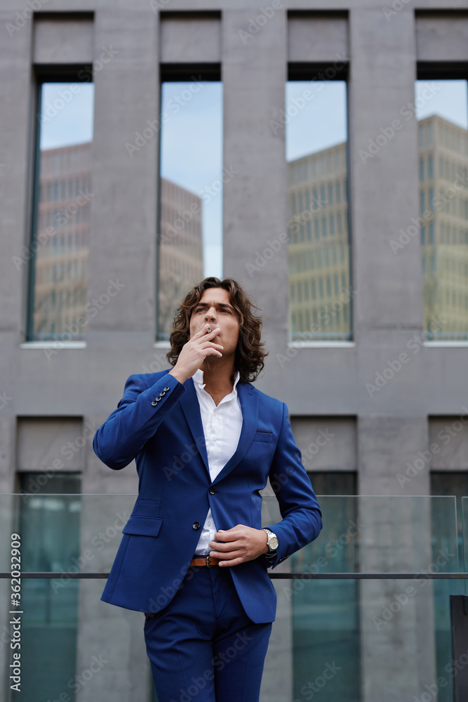 Portrait of wealthy confident gentleman smoking a cigarette standing near office building Portrait of wealthy confident gentleman smoking a cigarette standing near office building