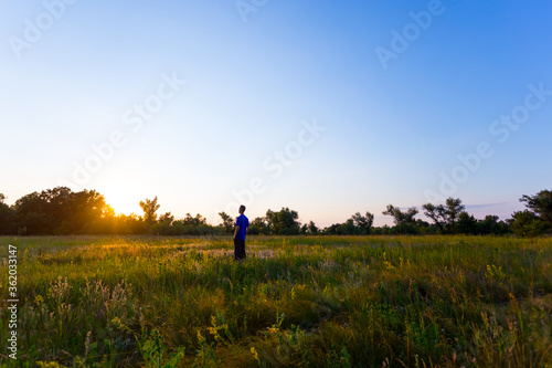 happy man see off evening sun among a green summer prairie, human emotion concept background