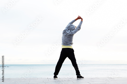 Full length portrait of athletic man doing warm up standing next to the beach before a run