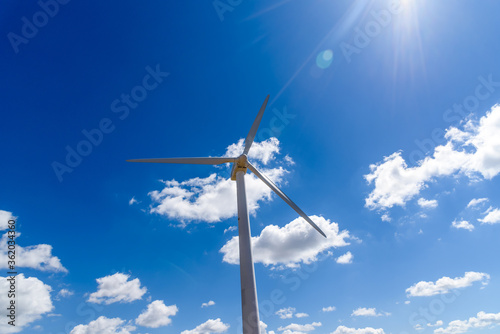 Low angle view of wind turbine for power generation against blue sky with sun flare. Concept eco clean energy production. Renewable energy