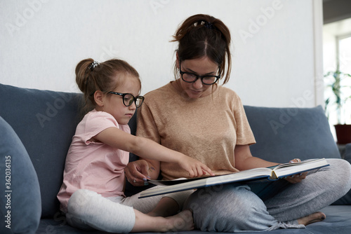 Mother and daughter are reading a book. Mother teaches a little girl.