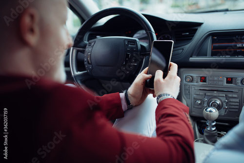 Man driving a car and holding mobile phone. Driver man using mobile phone while driving a car. © likoper