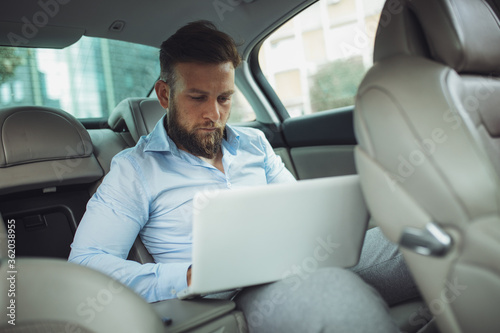 Young businessman working on laptop inside a car. A young businessman prepares for a meeting.