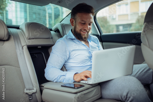 Young businessman working on laptop inside a car. A young businessman prepares for a meeting.