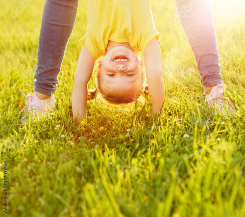 Portraits of a happy child standing upside down in the open air in the summer and sunlight, standing on his hands on the grass.