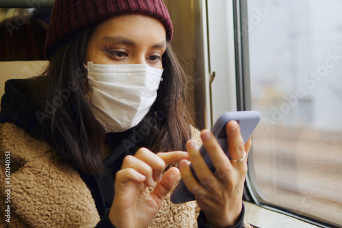 Young Asian Woman In Respirator Mask Using Smartphone In A Train. Ecological Pollution Air Infection Coronavirus Concept. Tokyo, Japan. photo