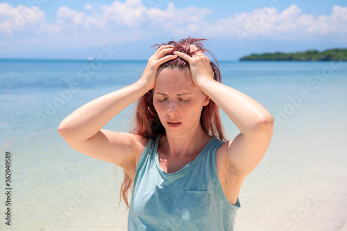 Woman with severe headache on vacation. Bright sun negative impact sunstroke. Medicine on summer photo