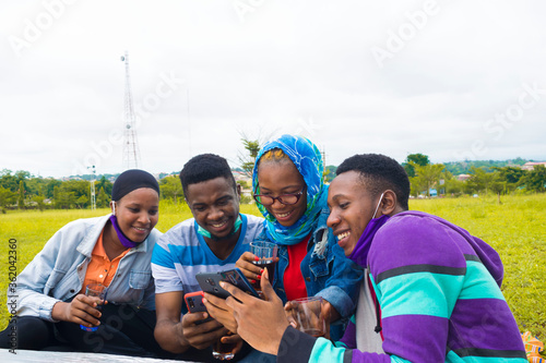 young black people sitting in a park, drinking from their glass cups and using smartphone