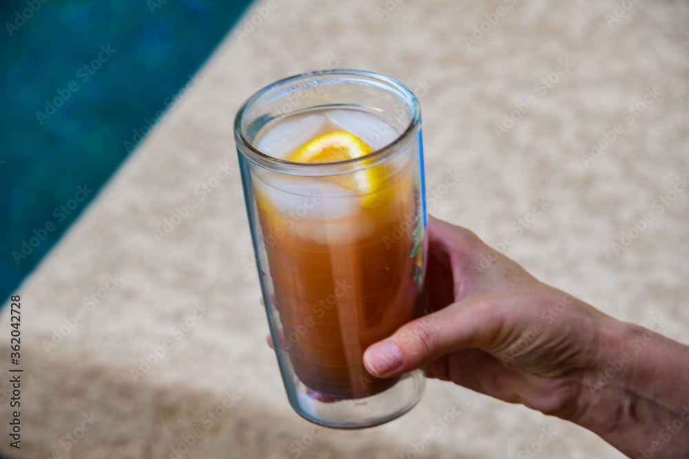 A person holding a class with a colorful  drink and lemon.