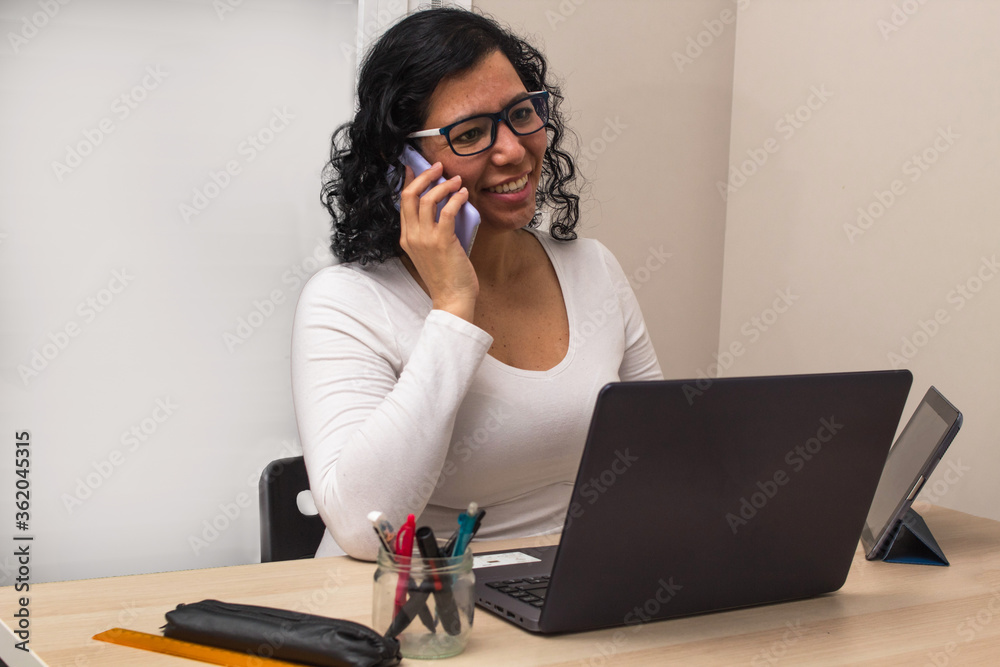 Young caucasian woman in a white shirt and glasses working with her laptop while talking on the mobile phone Young caucasian woman in a white shirt and glasses working with her laptop while talking on the mobile phone