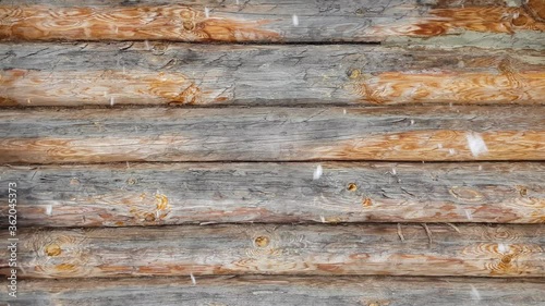 Falling snow on the background of a wooden log house. In winter, outdoors in the daytime. Round wooden logs connected by tow. Against the background of the wall, snow falls in large flakes. For relax.