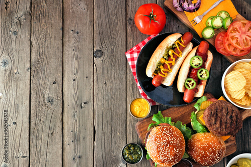 Summer BBQ food side border with hot dog and hamburger buffet. Overhead view over a dark wood background. Copy space.