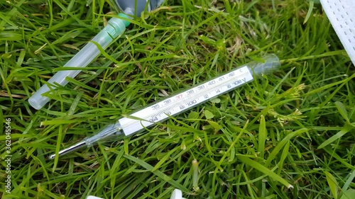 Close-up of essential drugs for the prevention of viral diseases: thermometer, disinfectant spray, syringe, medical face mask. Against the background of green grass on a sunny day