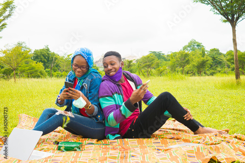 young black couples sitting down in a park, using their smartphones to surf the internet © Courage