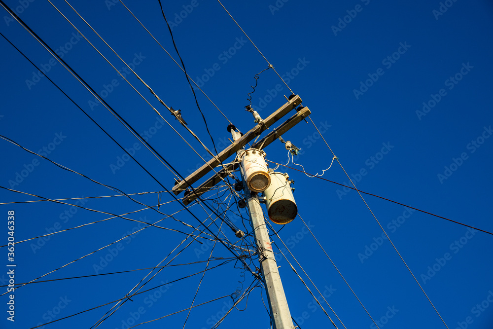 Electric wires and pillar on blue sky background. Tangle of electrical wires. Electric pillar with too many connection. Asian electric supply. Industrial electrification pole with wire and birds Electric wires and pillar on blue sky background. Tangle of electrical wires. Electric pillar with too many connection. Asian electric supply. Industrial electrification pole with wire and birds