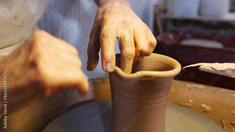 Close up of male potter shaping neck of clay vase on pottery wheel in ceramics studio - shot in slow motion