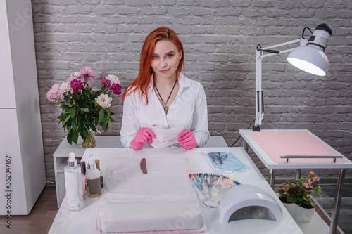 Red-haired girl manicure master sits in the office at the table and waits for his client. 