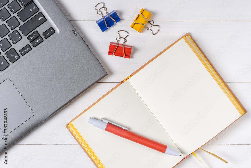 Working laptop on a white wooden table with notebook and paper clips