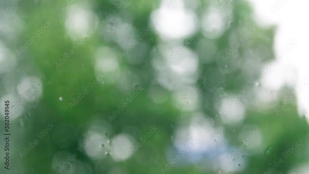 Closeup of rain on glass of window with green trees outside. Rain on the glass.