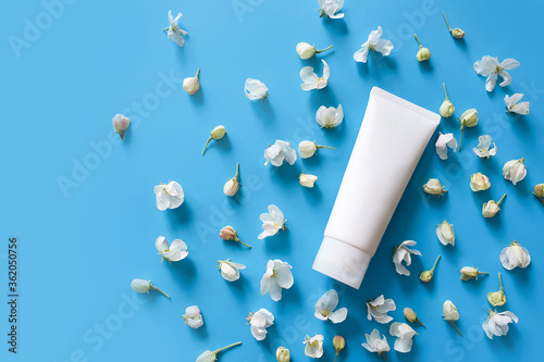 Top view of mock up of white squeeze bottle plastic tube for branding of medicine or cosmetics - cream, gel, skin care, toothpaste. Duds of blooming sakura on a blue background. Spa cosmetic product