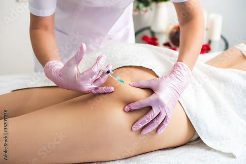 correction of body fat with lipolytics. in the cosmetologist’s office, female hands inject a young woman in the thigh.