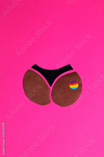 The black paper booties in bikini with a rainbow sign are cut out on a handmade pink background. The vertical photo of paper art was made for your craft design.