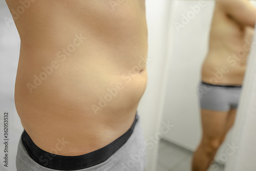 naked man body in underwear standing in front of mirror with big belly and visible love handles recognizing not being slim