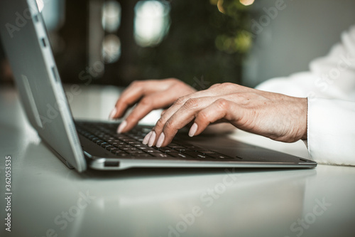 Female hands typing on laptop keyboard in office. Businesswoman working with computer. Close up shot. Tinted image.