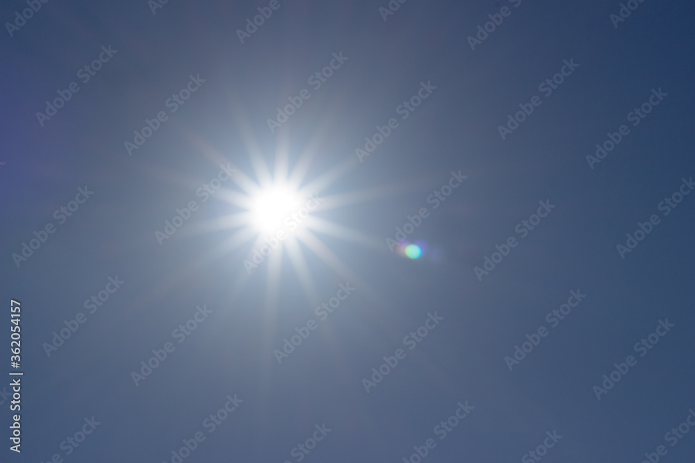 
bright sun in the blue sky, visible rays of the sun