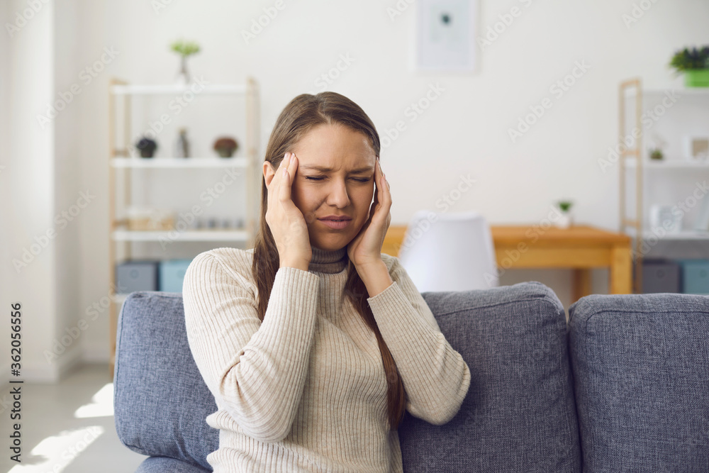 Headache. Migraine. A blonde woman has a headache while sitting on a sofa in a room. Headache. Migraine. A blonde woman has a headache while sitting on a sofa in a room.