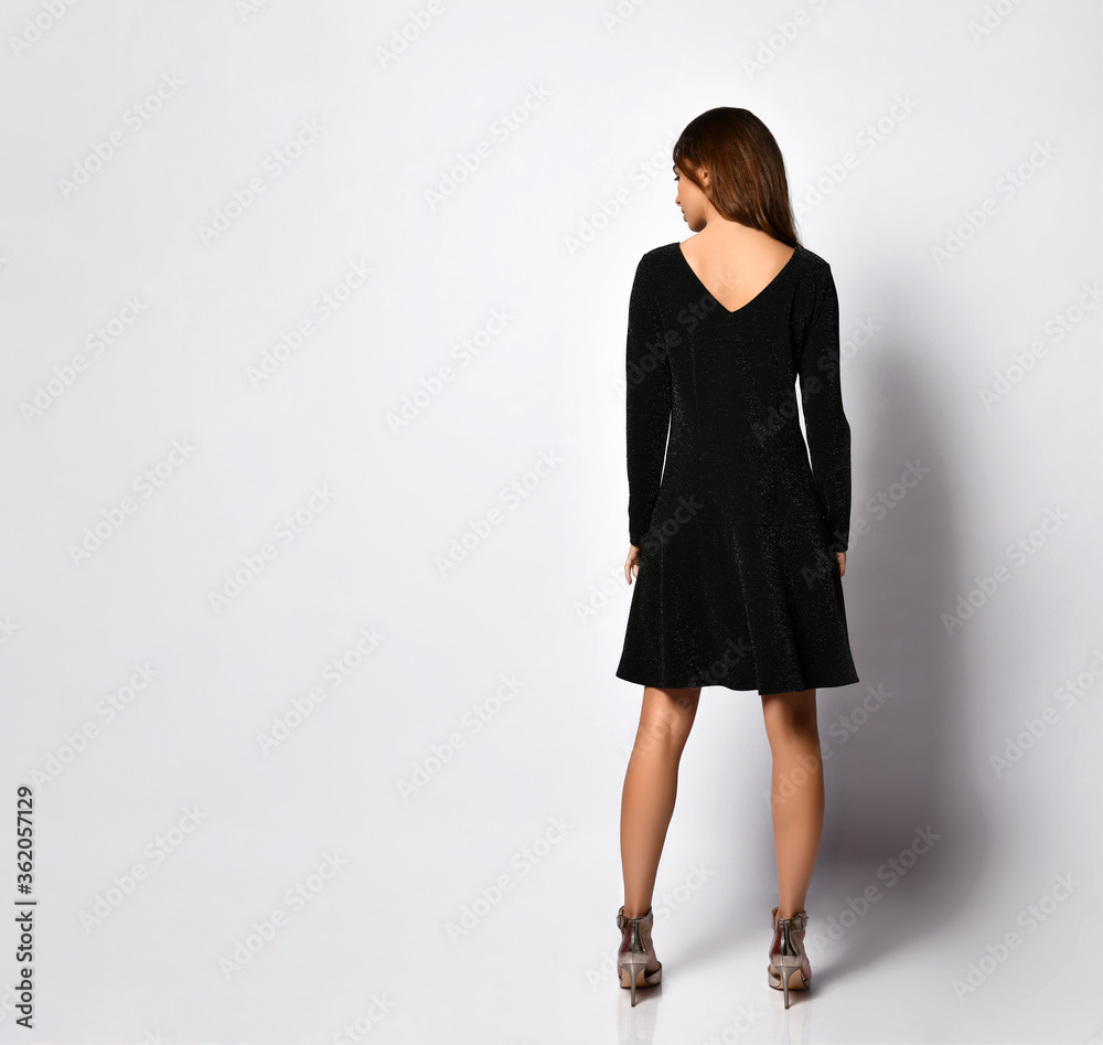 Rear view of a beautiful young female in glamour black minidress with a V-shaped neckline on back. Full length portrait isolated on white. Copy space Rear view of a beautiful young female in glamour black minidress with a V-shaped neckline on back. Full length portrait isolated on white. Copy space