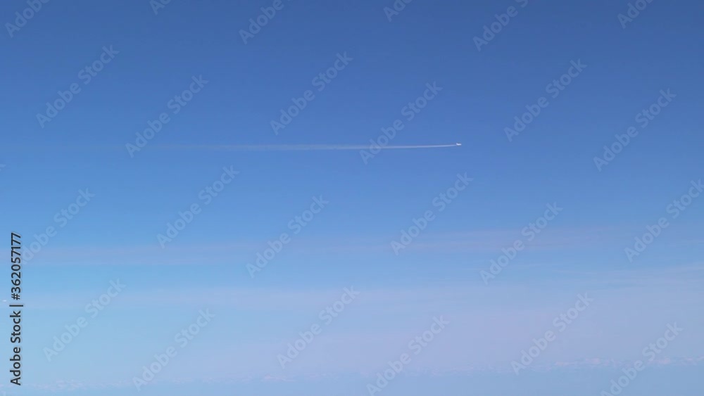 White trail from a flying airplane. Plane flying in the blue sky among clouds. White cloud lines made of aircraft.-Dan White trail from a flying airplane. Plane flying in the blue sky among clouds. White cloud lines made of aircraft.-Dan