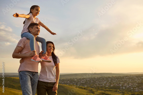 Daughter on the shoulders of parents watching the sunset on nature in the evening at sunset.